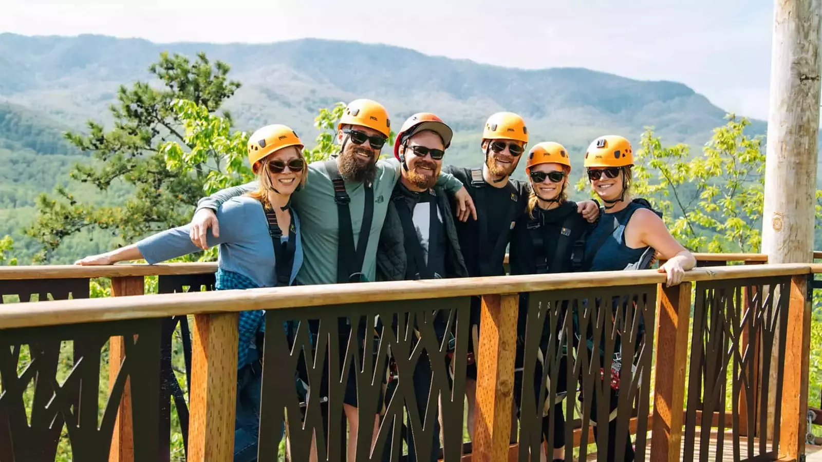group of zipliners smiling on ziplining platform with mountains in background
