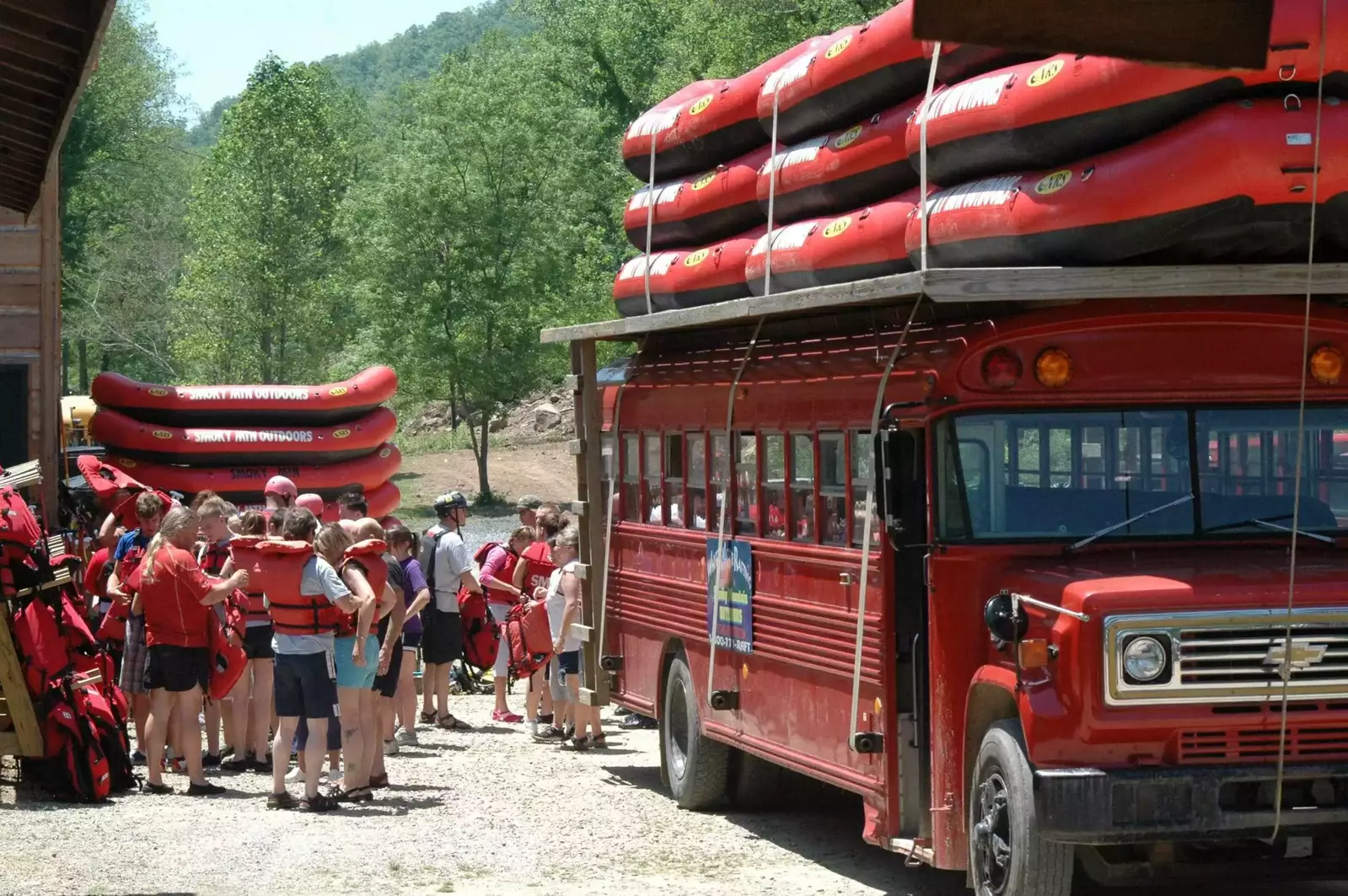 rafters boarding red bus with red rafts on roof