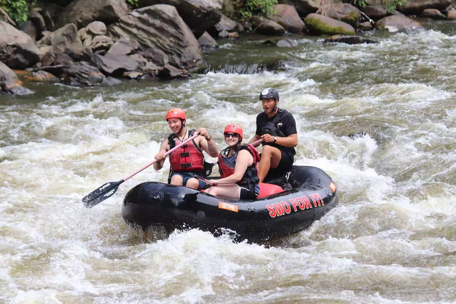 black raft with two people plus guide going through rapids