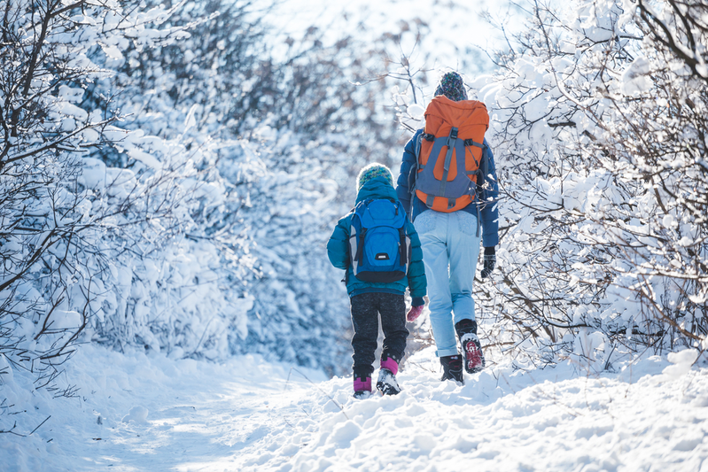 parent and child hiking along a snowy trail while dressed in warm clothes and wearing backpacks