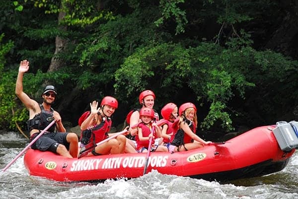 Happy family waving while enjoying white water rafting near Pigeon Forge